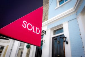 Estate,Agent,Sold,Sign,With,Houses,In,Background
